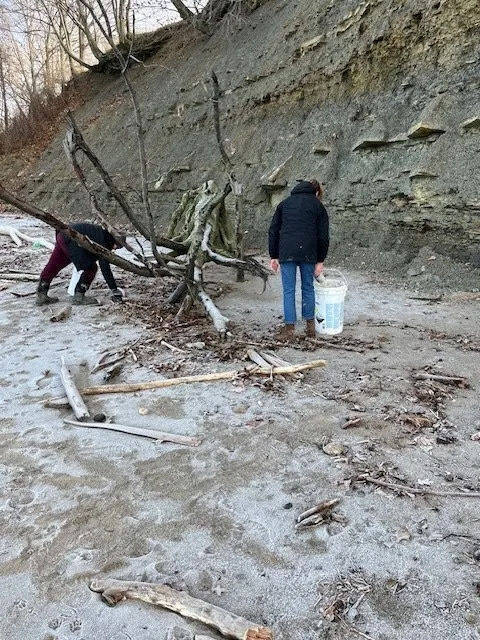 Two people with their backs to the camera looking down at the beach with buckets in hand.